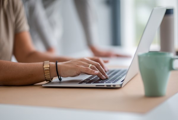 Kvinnliga händer  skriver på laptop, en grön kaffekopp står bredvid