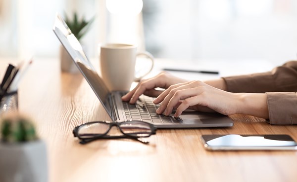 Händersom skriver på laptop, glasögon ligger bredvid